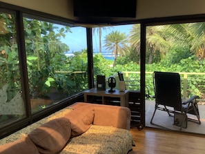 Relax in a serene space with a view of lush greenery and a palm tree, featuring a sofa, a table with a speaker and headphones, and a chair.