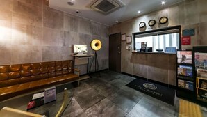 A modern reception area with a leather bench, a desk with a computer, and a wall-mounted clock. - HOTEL 385 (Changwon)