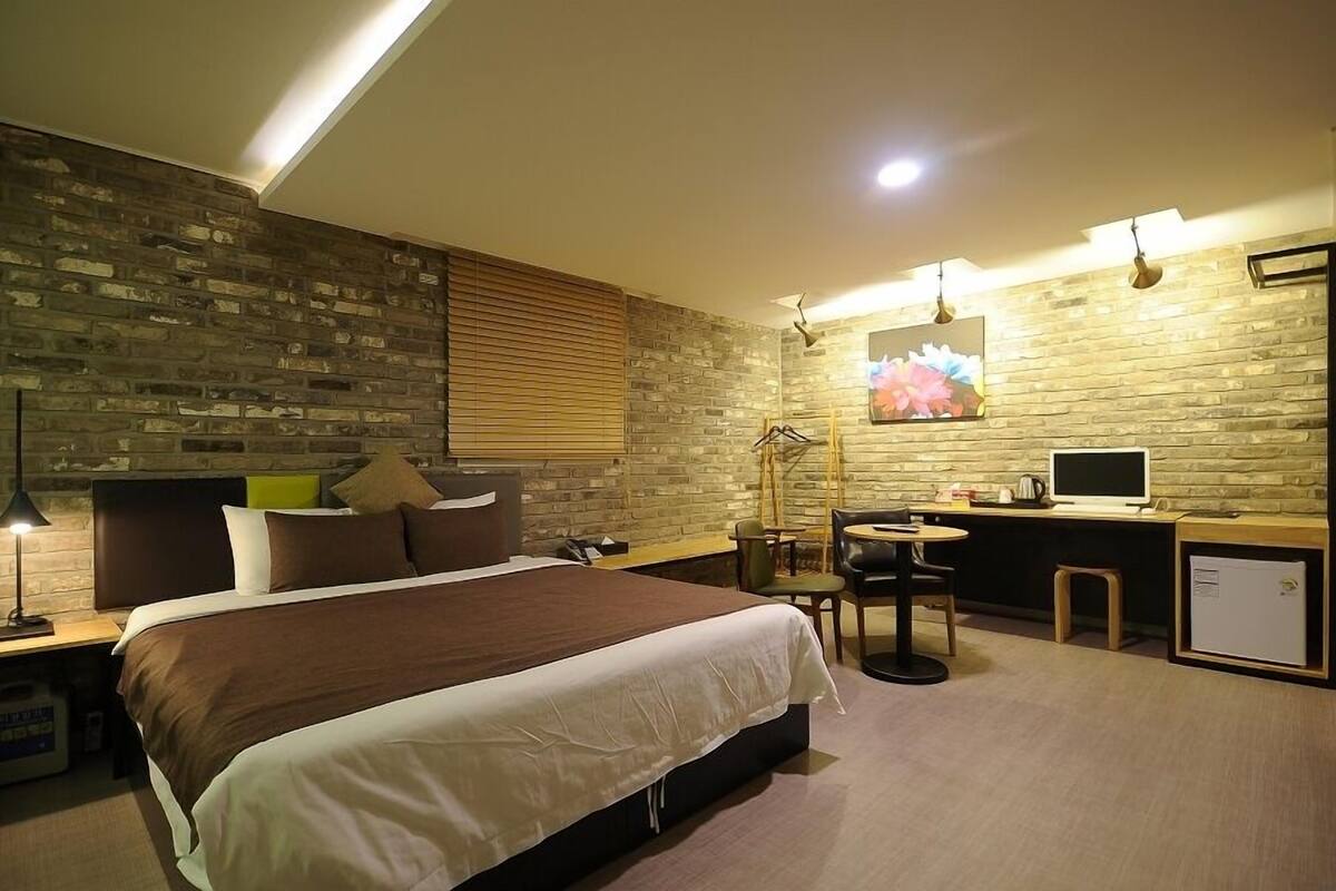 A modern hotel room with a large bed, a desk with a computer, and a small seating area.