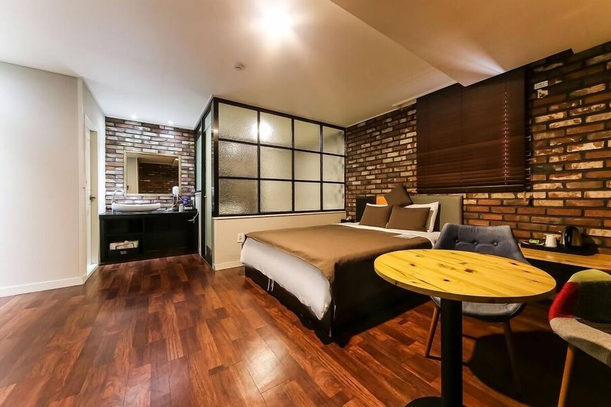 A compact room with a bed, a small round table, and a sofa. There is a window with a view of a brick wall outside.