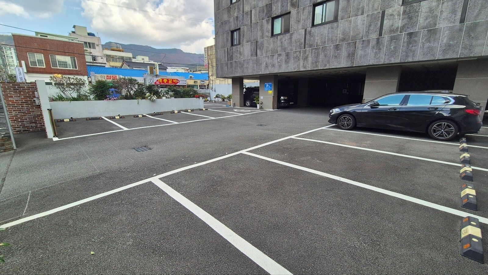 A parking lot with marked spaces, a black car parked, and a building with a sign that reads "HOTEL".