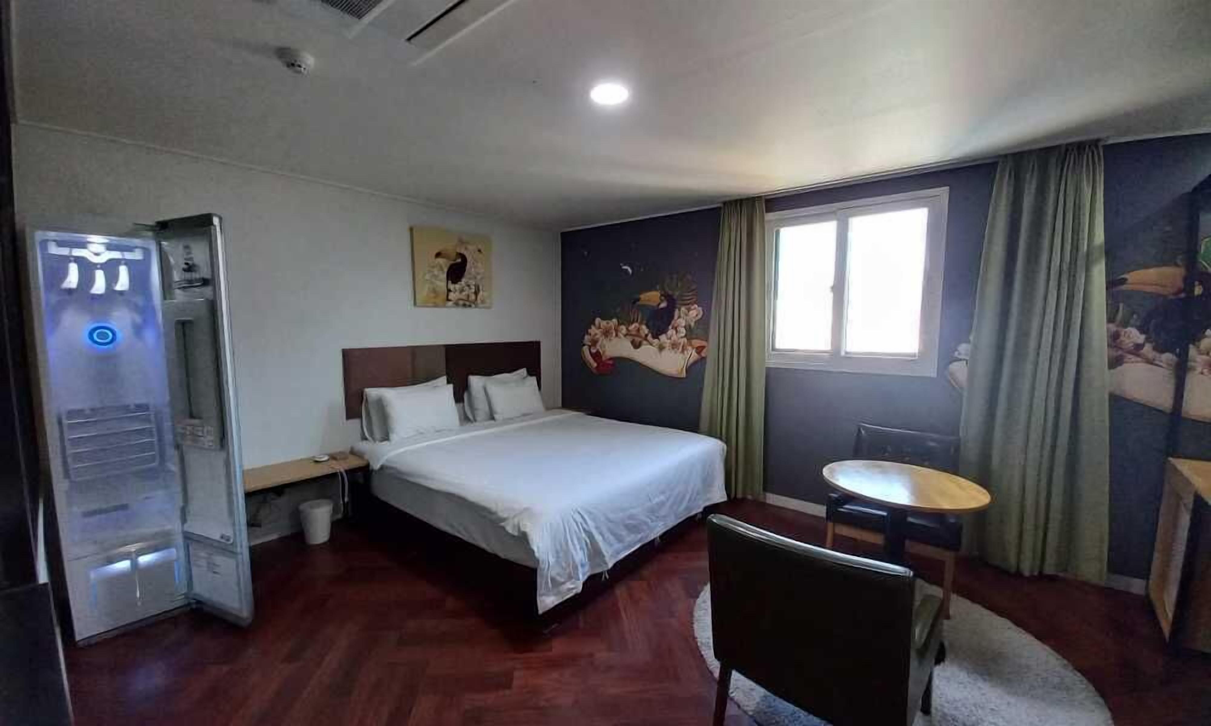 A hotel room with a bed, a desk, a chair, a window, and a painting on the wall.