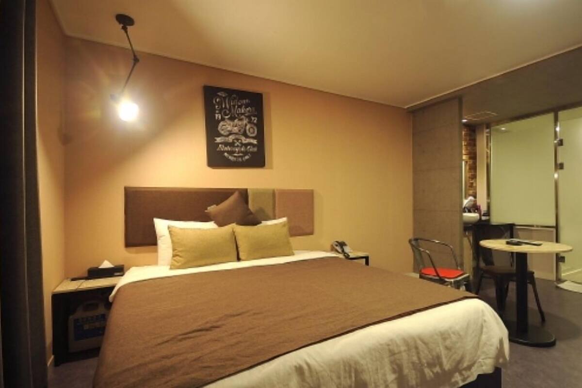 A hotel room with a large bed, a bedside table, a chair, a small table, and a mirror.