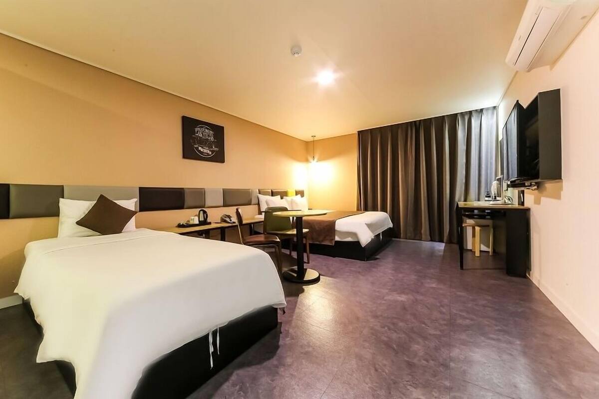 A hotel room with a large bed, a desk, a chair, a TV, and a wall-mounted air conditioner.