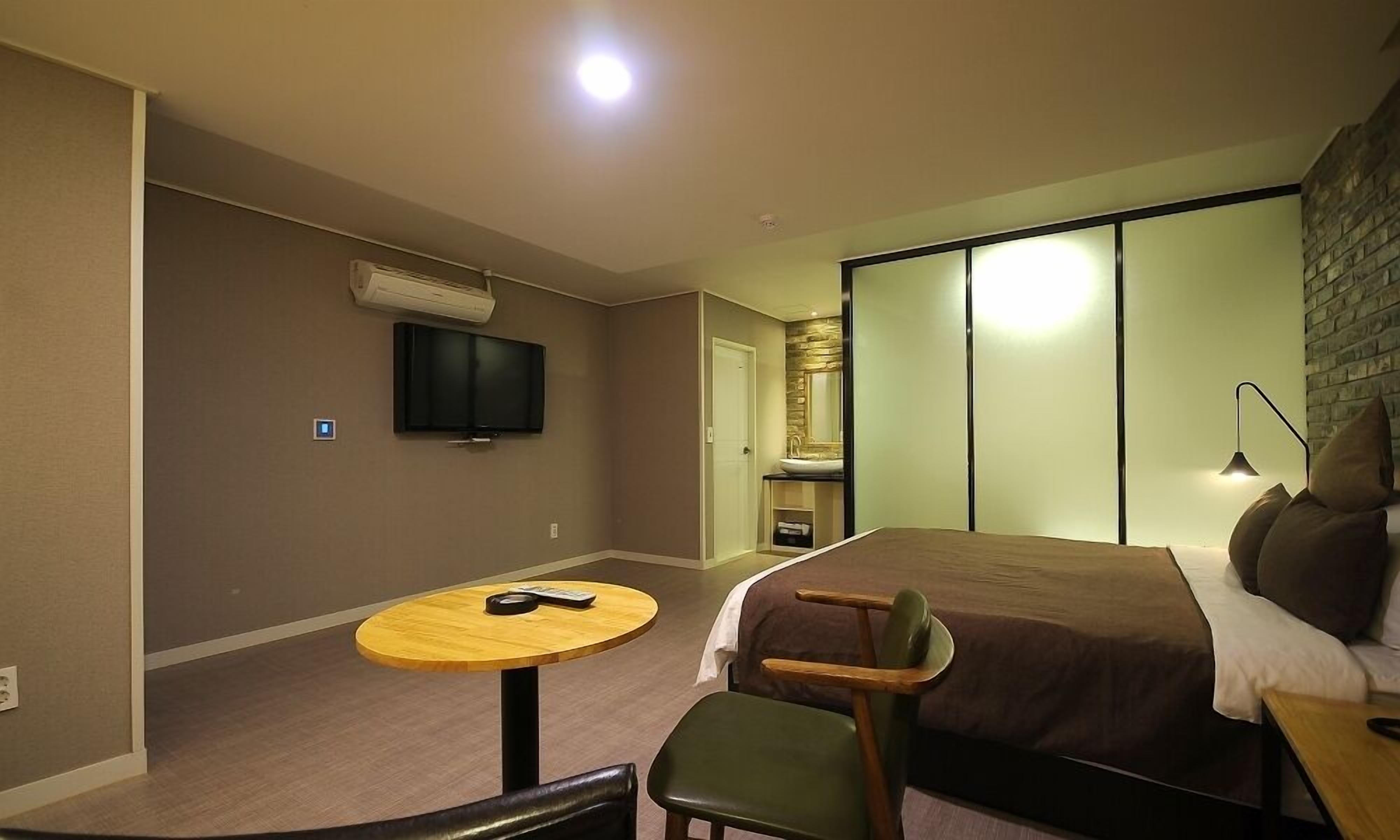 A hotel room with a bed, a TV mounted on the wall, a small round table, and a chair.