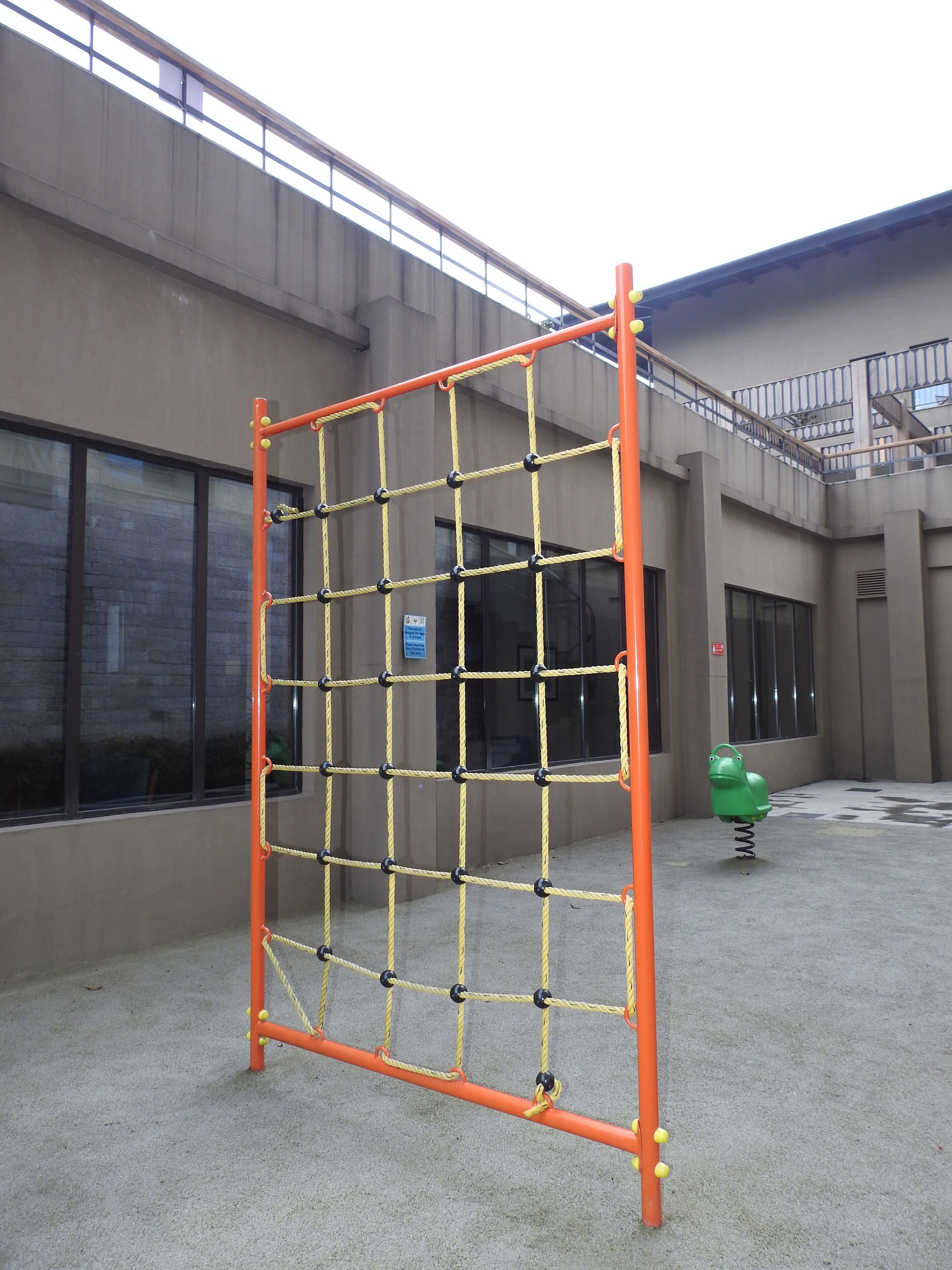 Una estructura de juegos con una red de cuerdas y un columpio con forma de rana verde.