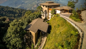 A hillside property with multiple buildings, including a prominent tower-like structure, surrounded by lush greenery and overlooking a mountainous landscape. - Taj Guras Kutir Resort & Spa, Gangtok (Gangtok)