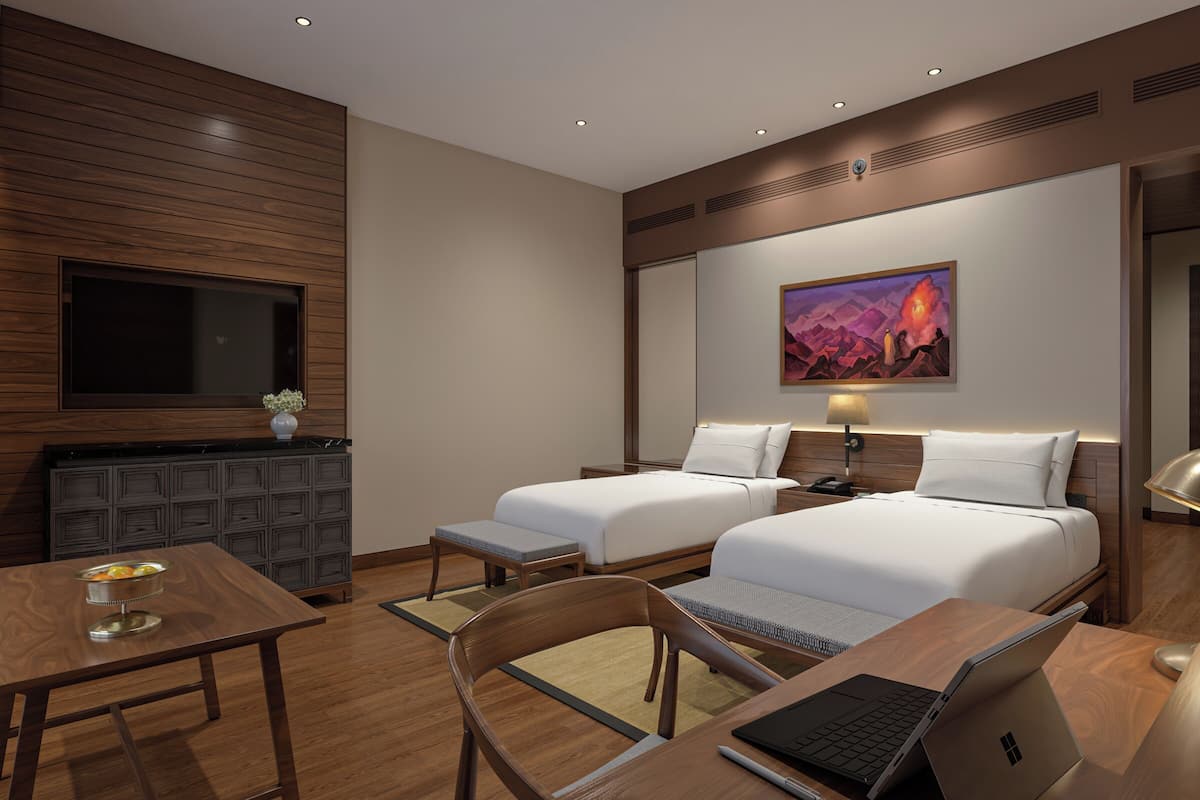 Een hotelkamer met twee bedden, een bureau met een laptop, een televisie en een schilderij aan de muur.