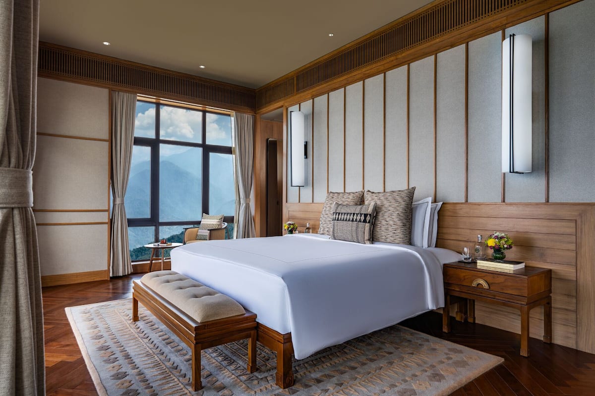 Een moderne hotelkamer met een groot bed, een houten hoofdeinde en uitzicht op bergen.