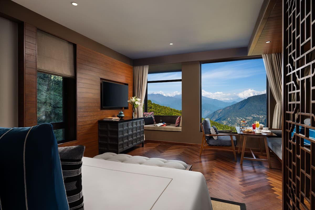 Een moderne woonkamer met een groot raam met uitzicht op de bergen, een flatscreen televisie aan de muur en een eethoek met een tafel en stoelen.