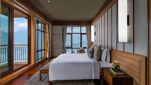 A spacious bedroom with a large bed, a bedside table with a vase of flowers, and a view of the mountains through large windows. - Taj Guras Kutir Resort & Spa, Gangtok (Gangtok)