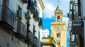 Une rue étroite bordée d’immeubles dotés de balcons et surmontée d’une tour imposante coiffée d’une croix.