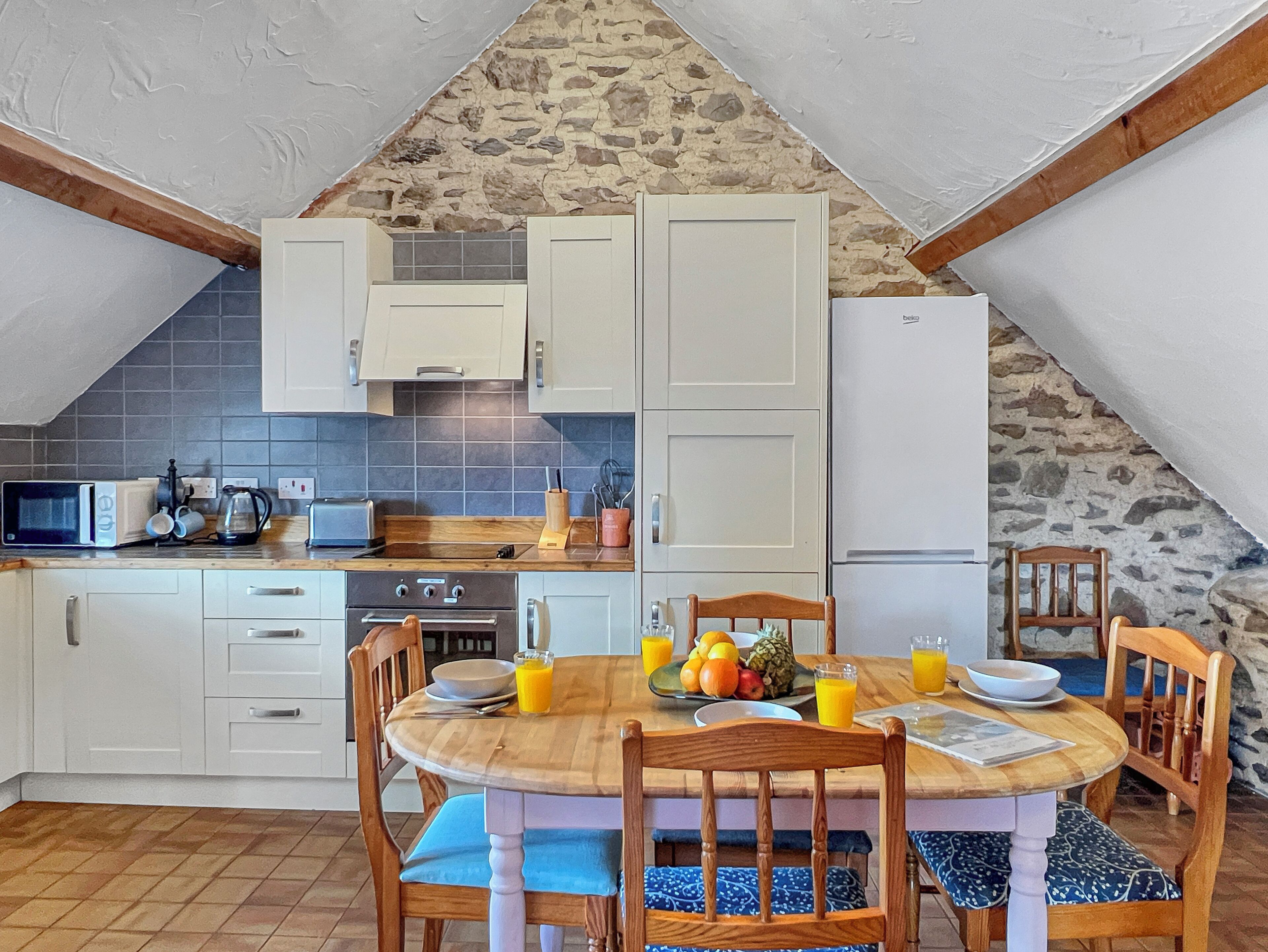 Una cocina con alacenas blancas, una pared de piedra, una mesa de comedor de madera y un microondas.