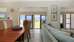 A dining area with a wooden table and wicker chairs, a sofa, and a view of the outdoors through glass doors.