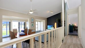 A spacious living area with a balcony, a dining area with wicker furniture, and a TV in the background.