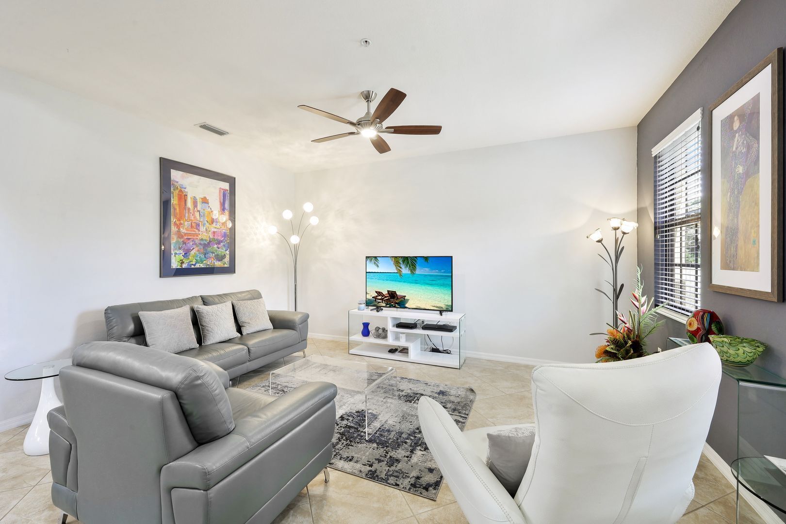 A modern living room with a grey sofa, a white armchair, a flat-screen TV, and a ceiling fan.
