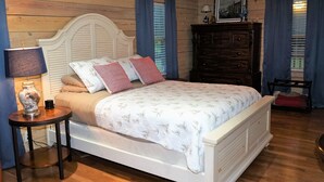 A bedroom with a wooden headboard bed, a nightstand with a lamp, a dresser, and a ceiling fan. - Secluded, peaceful Coastal Log Cabin with hot tub. (Townsend)