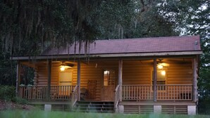 A log cabin with a porch, wooden railings, and two illuminated windows. - Secluded, peaceful Coastal Log Cabin with hot tub. (Townsend)