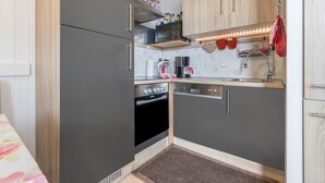 A compact kitchen with grey cabinets, a microwave, a coffee maker, and a dishwasher. - Holiday Apartment "Harzblick" with Mountain View, Balcony & Wi-Fi (Altenau)