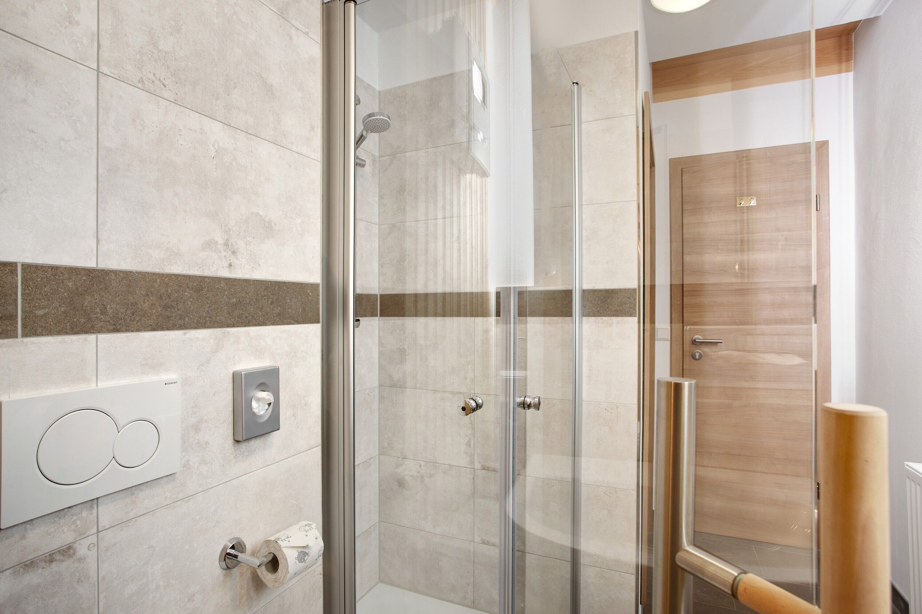 A modern bathroom with a glass shower enclosure, a wooden door, and a towel rack.