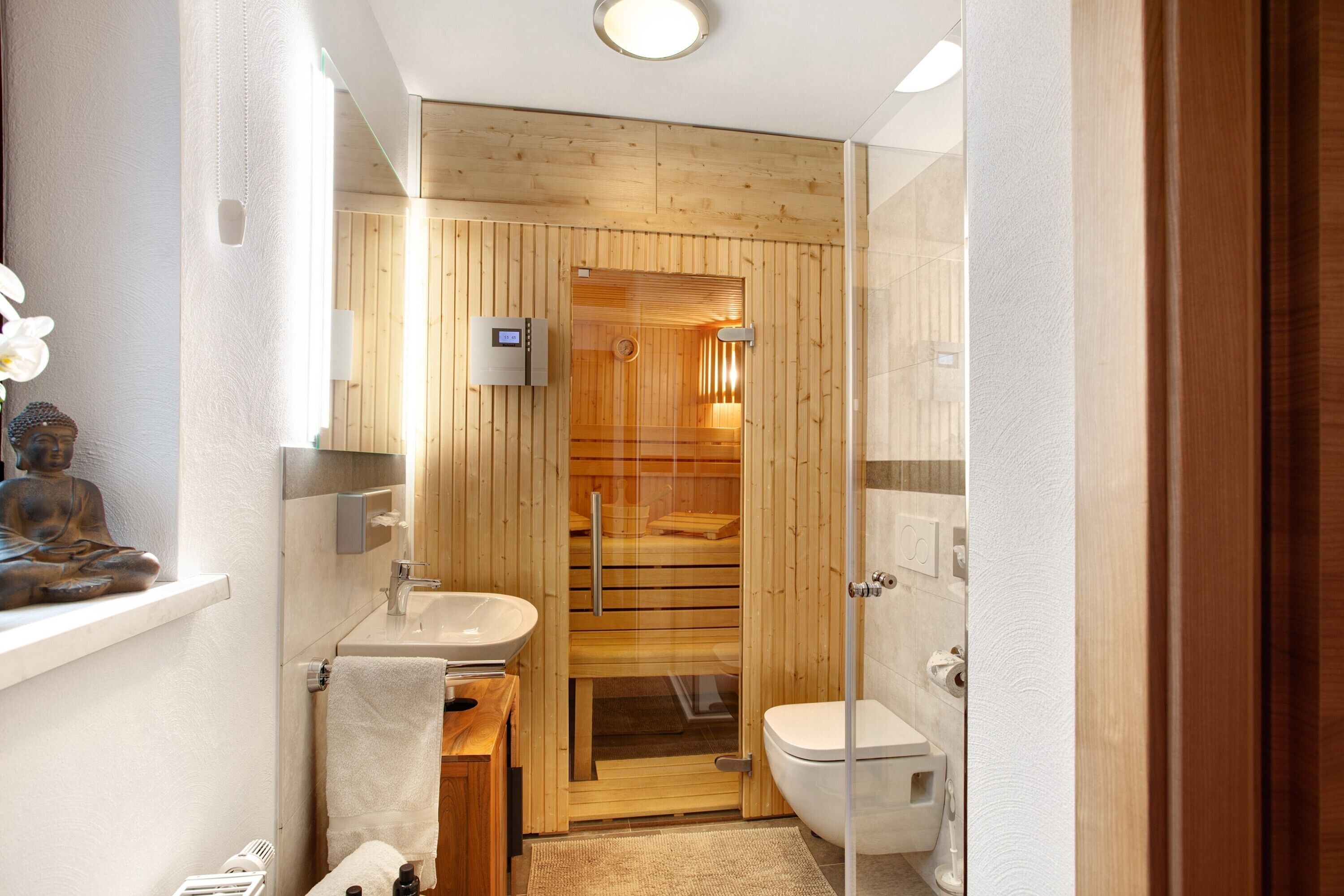 Ein modernes Badezimmer mit einer Wand aus Holzpaneelen, einer Saune mit Glastür, einem weißen Waschbecken und einer Toilette.