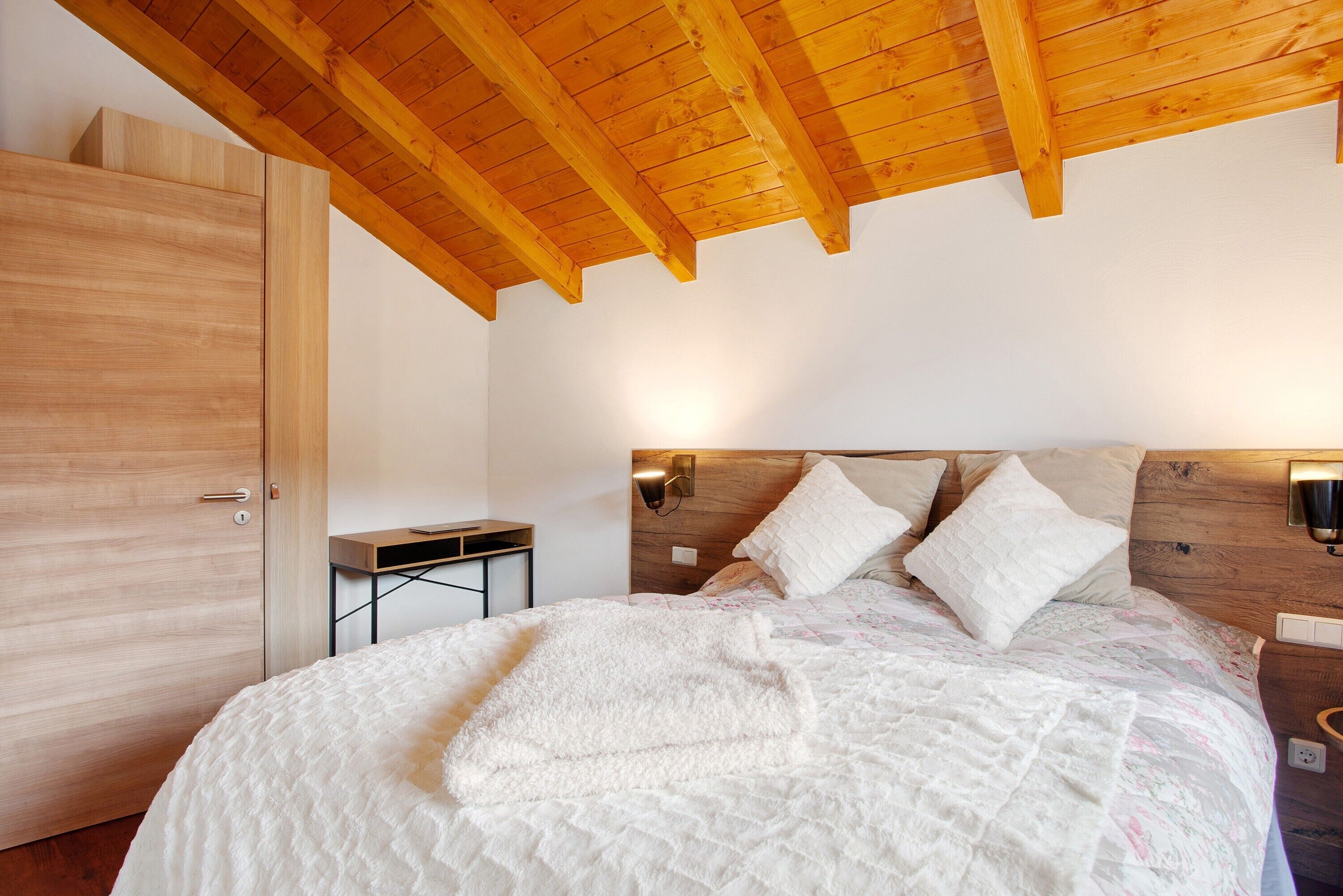 A bedroom with a wooden ceiling, a bed with white bedding, a nightstand, and a wooden wardrobe.