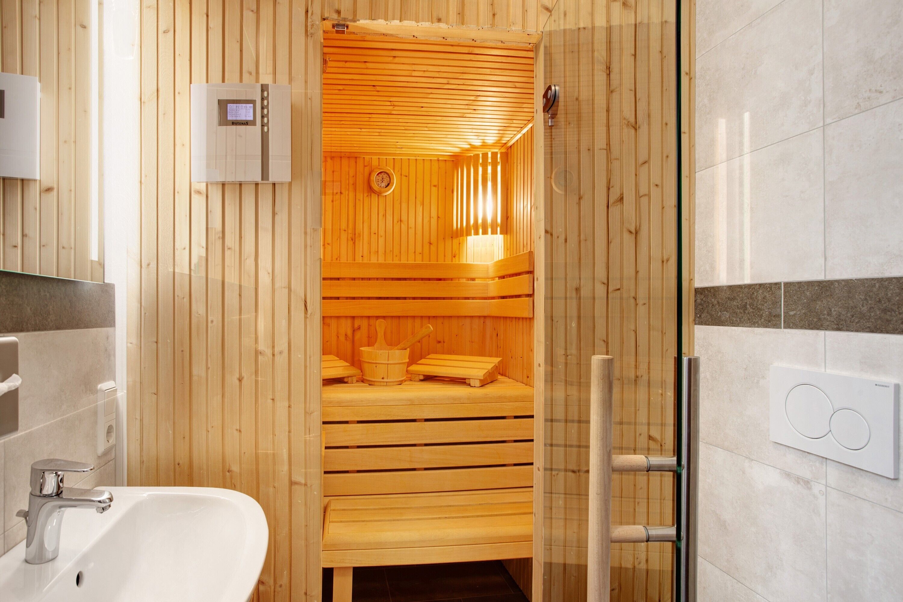 Un sauna avec des bancs en bois, un panneau de commande et une porte en verre.