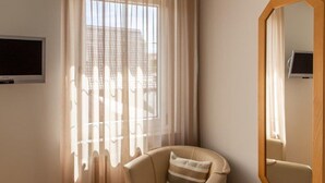 Una habitación con un ventanal grande, una silla, un televisor y un espejo.