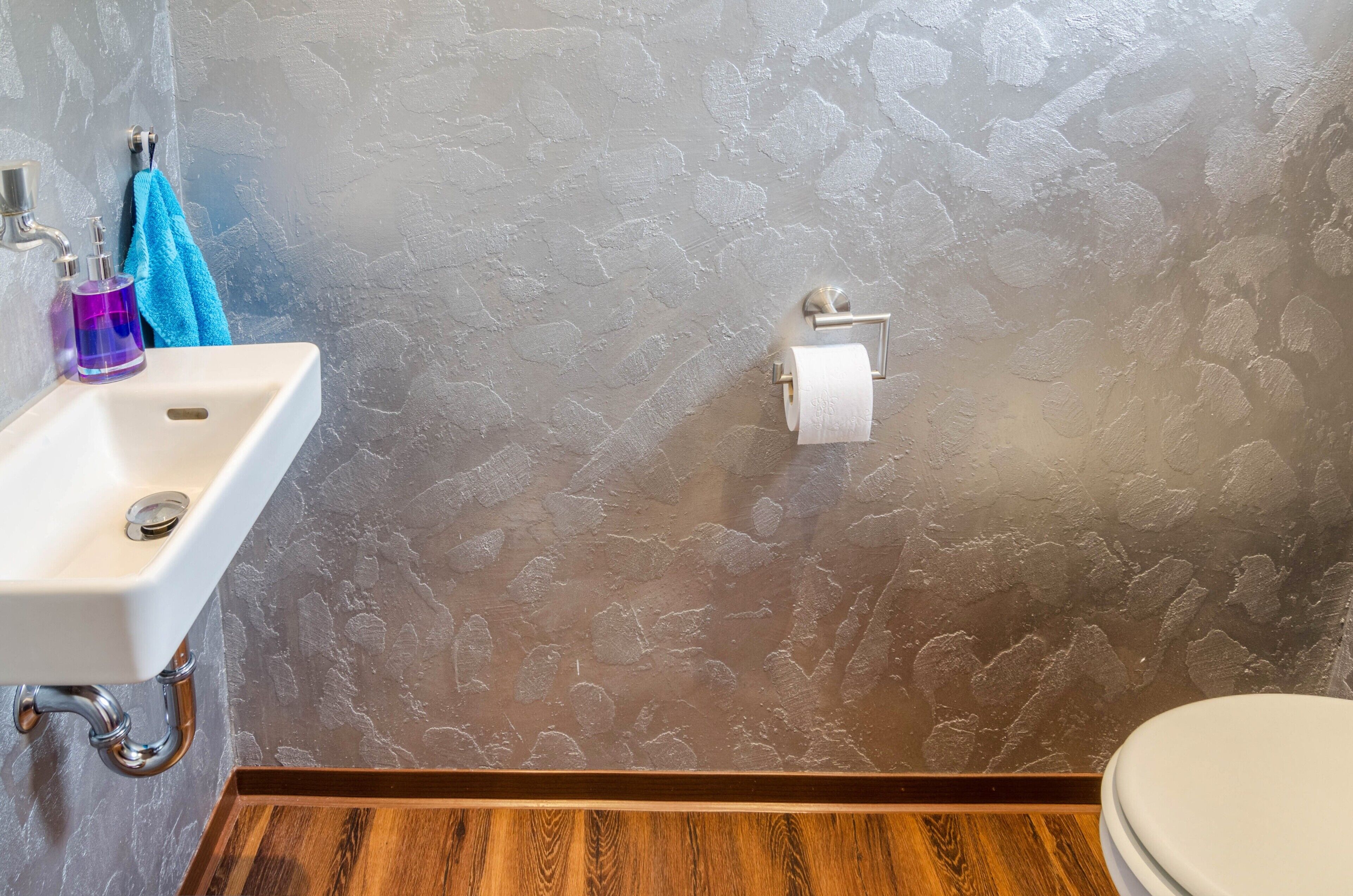 Ein Badezimmer mit weißem Waschbecken, Toilette und einer Wand mit Struktur.