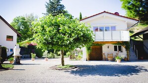 Un bâtiment à deux étages doté d’un balcon, entouré d’une cour en gravier et agrémenté de plantes en pot.