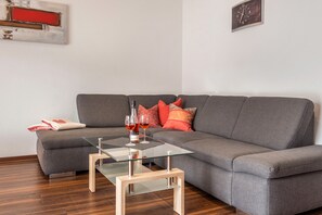 Una sala moderna con un sofá gris, una mesa de centro de vidrio y una mesita auxiliar de madera.