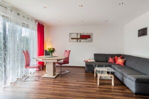 Una sala de estar moderna con una mesa de comedor, sillas rojas, un sofá gris y una mesa de centro de vidrio.