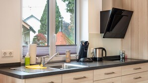 A modern kitchen with a built-in sink, wooden cabinets, and a window overlooking a residential area. - Holiday Home with Balcony, Terrace, Private Patio, Shared Garden and Wi-Fi (Salem)