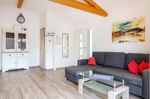 Un salon moderne avec un canapé gris, des coussins rouges, une table basse en verre, un meuble blanc et un tableau accroché au mur.