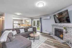 Una sala moderna con un sofá seccional gris, una mesa de centro redonda y una chimenea.