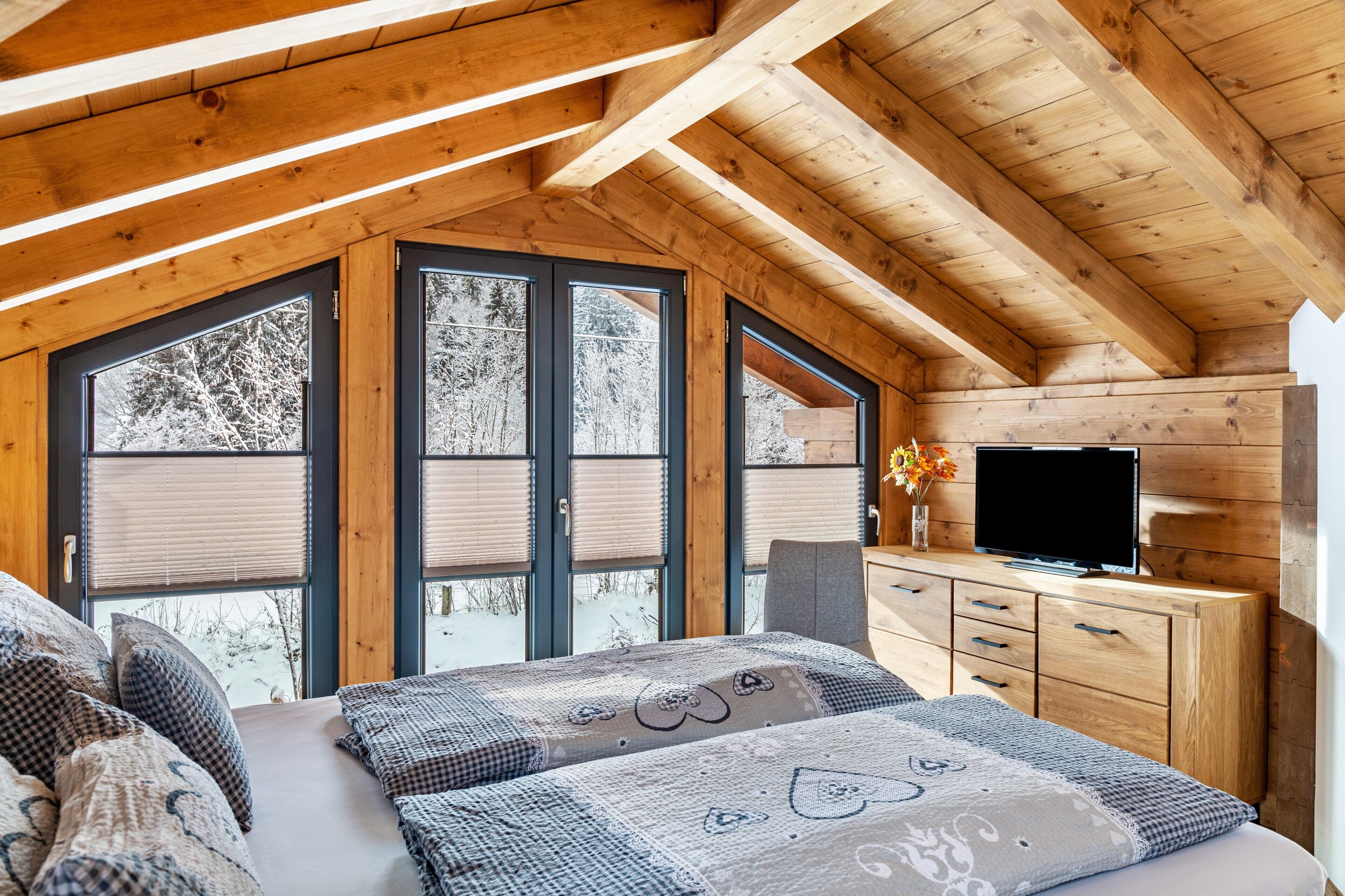 Un dormitorio rústico de cabaña de troncos con una cama, un aparador, un televisor y ventanas amplias.