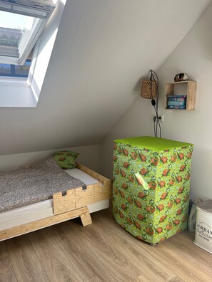 Un apartamento pequeño de una sola habitación con techo estilo loft, una cama con estructura de madera, un mueble de almacenamiento con diseño verde, un estante con libros y una ventana con persianas.