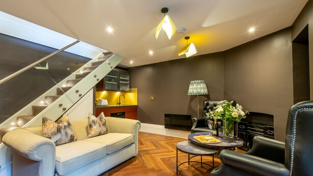 A modern living room with a sofa, a coffee table, a fireplace, and a staircase.