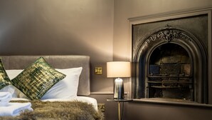 A room with a bed, green pillows, a fur throw, a lamp, and a fireplace.