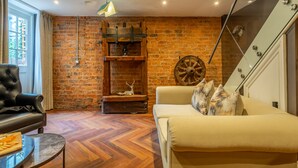 A cozy living room with a brick wall, a leather sofa, a glass coffee table, and a wooden fireplace.