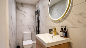 A modern bathroom with a white toilet, a vanity with a gold faucet, and a mirror with a gold frame.