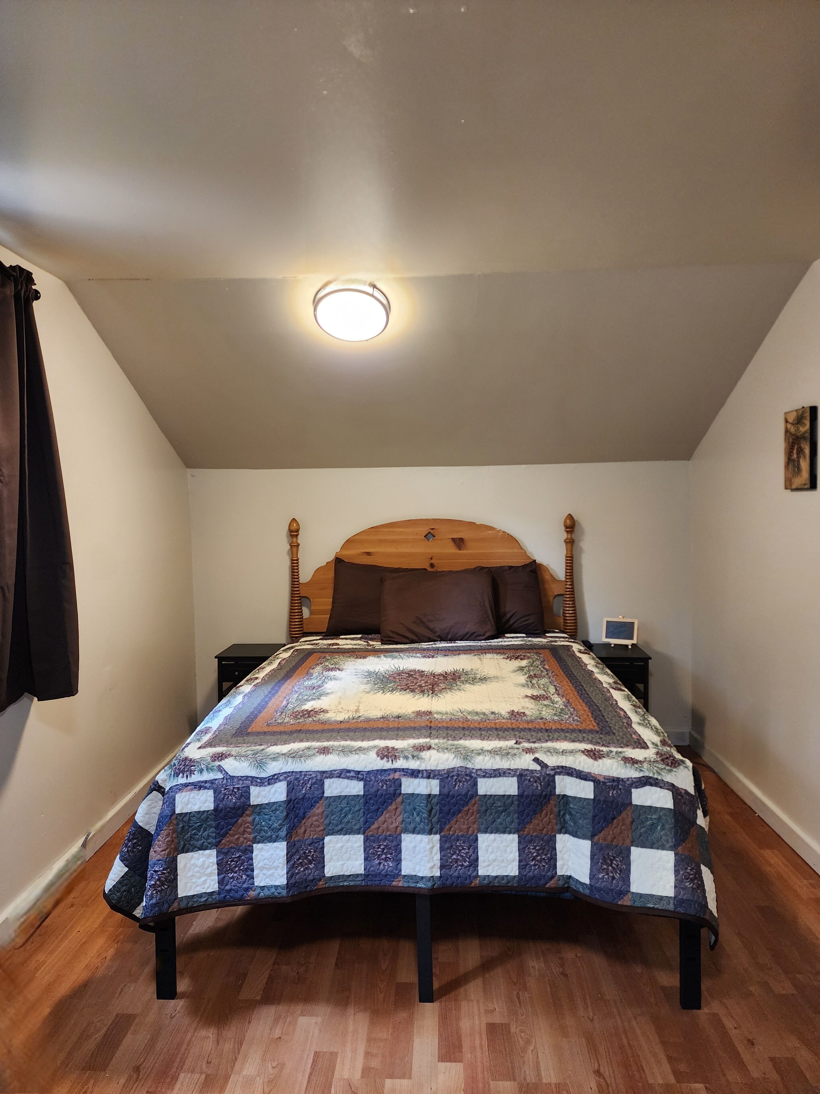 Un dormitorio con estructura de cama de madera, colcha acolchada, una mesita de noche y estante fijado a la pared.