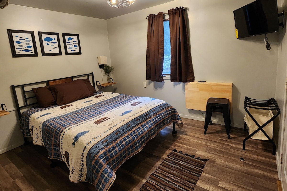 A bedroom with a bed, a desk, a chair, a TV, and a window with curtains.