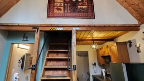 A wooden staircase leading to a kitchen with a chandelier and a decorative wall hanging. - Bear Necessities Cottages (Seward)