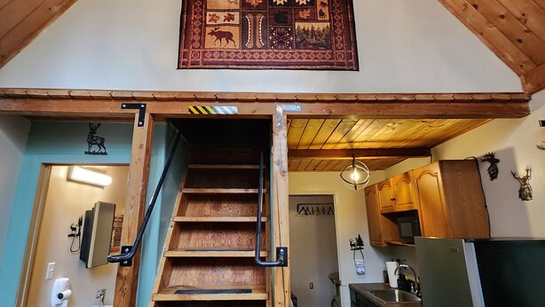 A wooden staircase leading to a kitchen with a chandelier and a decorative wall hanging. - Bear Necessities Cottages (Seward)