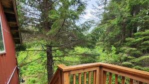 A wooden deck with a chair and a table, overlooking a forested area. - Bear Necessities Cottages (Seward)