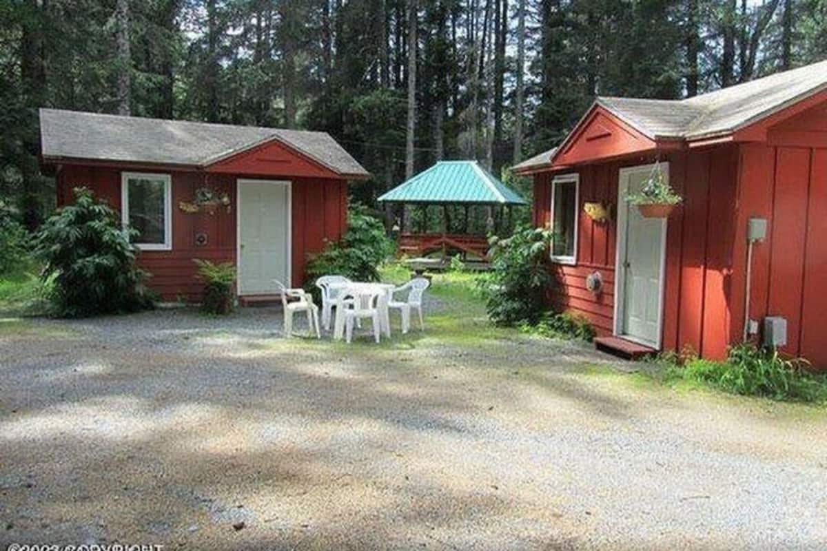 A rustic cabin area with two small cabins, a covered picnic table, and a gravel driveway.