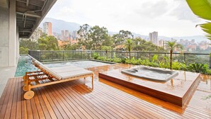 A wooden deck with a hot tub and lounge chairs overlooking a cityscape and mountains.