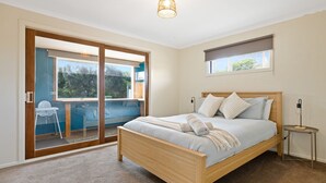 Une chambre avec un lit en bois, une petite table de chevet, une fenêtre donnant sur un paysage agréable et une porte-fenêtre coulissante qui mène à un espace extérieur.