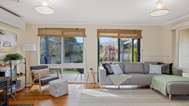 Un salon moderne avec un canapé gris, un pouf et une table basse en bois. Il y a deux grandes fenêtres à cadre bleu qui donnent sur le jardin.